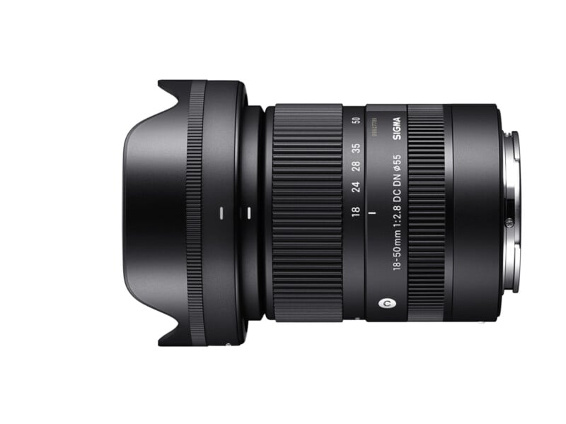 A Sigma 18-50mm f/2.8 DC DN lens in black, showing its side profile. The lens has a wide base with a ridged focus and zoom rings, and product labels indicating its specifications and brand. The background is white.