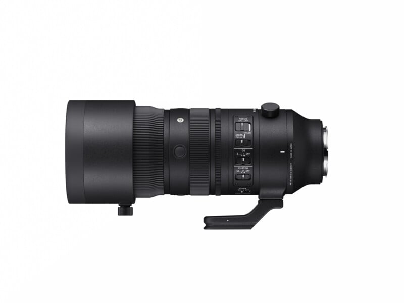 A black Sigma telephoto camera lens with a tripod mount, viewed from the side. The lens features various control switches and a textured grip section.