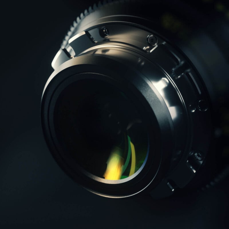 Close-up of a camera lens with a metallic body and detailed grooves, set against a dark background. The glass elements within the lens reflect light, showing subtle hues of green and yellow. The focus is on the lens's intricate construction and reflections.