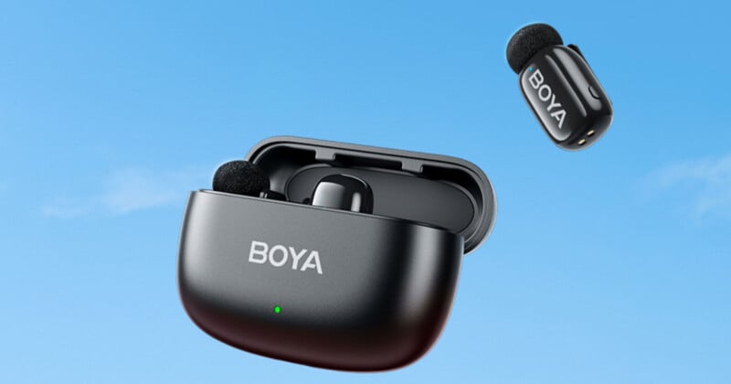 A pair of black wireless earbuds is shown against a blue sky. One earbud is in the open charging case, and the other is floating above. The case and earbuds have "BOYA" written on them.