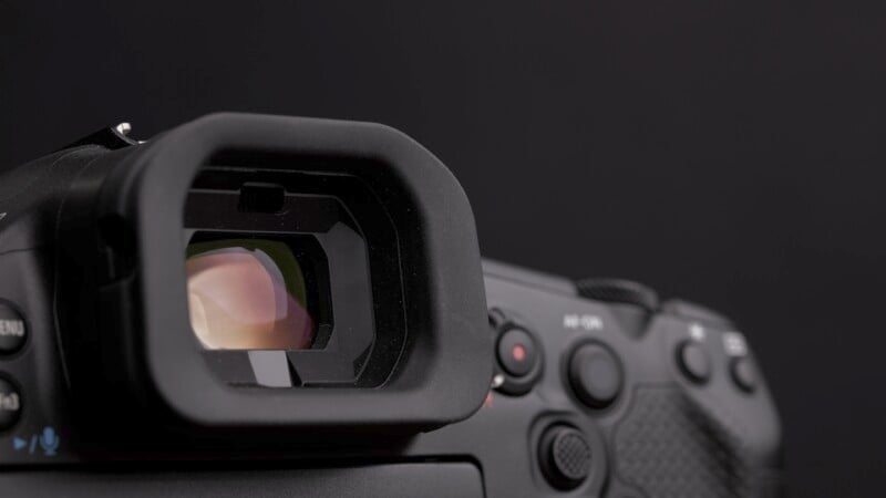 Close-up of a digital camera's viewfinder and control buttons against a dark background. The viewfinder is prominent, with light reflecting off the glass. The camera body appears detailed, showing various buttons and textured surfaces.