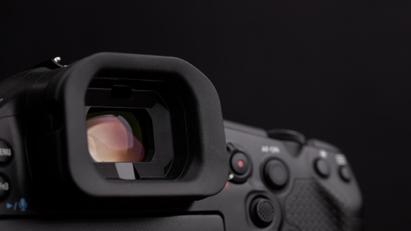 Close-up of a camera viewfinder and control buttons against a dark background. The focus is on the eyepiece, showing the camera's details and texture.