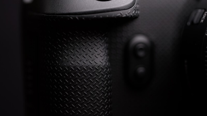 Close-up of a textured black camera grip and button, showing the fine pattern and detail on the camera surface. The image is focused on capturing the tactile design often found on professional camera equipment.