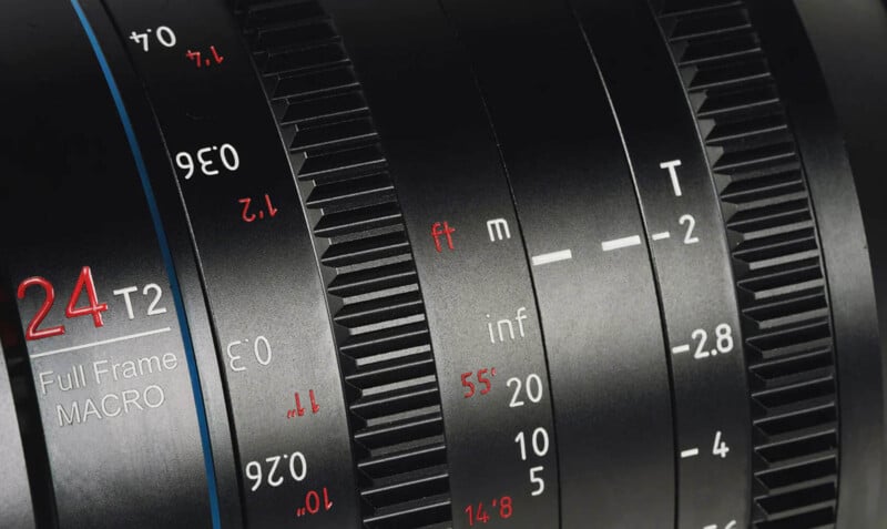 Close-up of a camera lens featuring detailed markings. The lens has a focal length of 24mm, a T-stop of T2, and other indicators in white and red lettering for distance in feet and meters, as well as aperture and focus ring settings. The black lens has a sleek design.