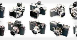 A collection of vintage cameras displayed against a white background. The assortment includes various models with black and silver bodies, lenses, and different viewfinder designs, showcasing the evolution of camera technology.