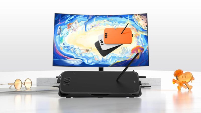 A digital art workstation featuring a drawing tablet with a stylus in front of a curved monitor displaying colorful artwork. On the desk are glasses, a laptop, and a decorative golden dog figure.