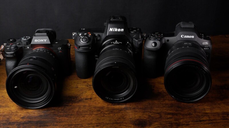 Three professional cameras with lenses are placed on a wooden surface against a dark background. The brands, from left to right, are Sony, Nikon, and Canon.