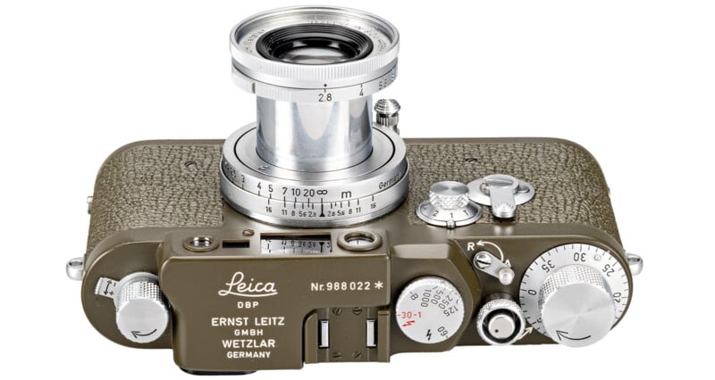 A vintage Leica camera with a brown textured body and a silver lens. The top surface features various knobs and dials for adjusting settings, and the brand name "Leica" is engraved.