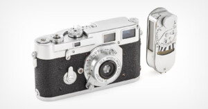 A vintage 35mm rangefinder camera with a black textured body and silver accents is shown. It's accompanied by a detachable light meter on the side. The camera has dials and a viewfinder on the top.