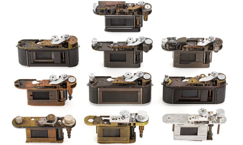 Nine vintage camera bodies are arranged in three rows, showcasing a variety of mechanical components and finishes. Each camera is partially disassembled, revealing internal mechanisms and detailing. The background is a plain white surface.