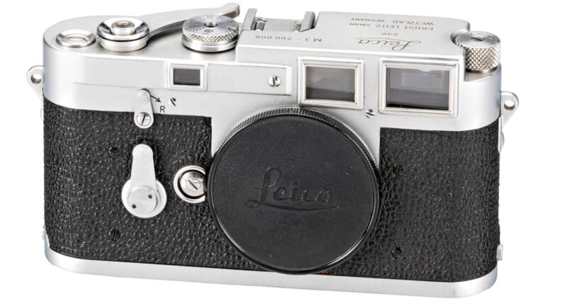 A vintage Leica M3 camera with a black body and silver detailing. The lens cap is on, and it features various dials and levers. The camera has a classic, retro design.