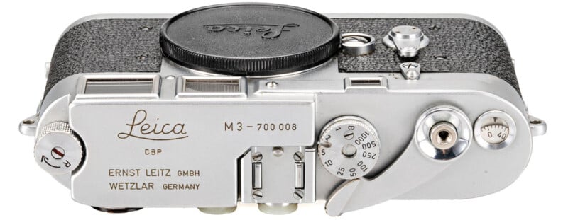 Top view of a vintage Leica M3 camera. The silver body features dials and levers for adjusting settings. The camera is labeled with "Leica" and "Ernst Leitz GmbH, Wetzlar, Germany.