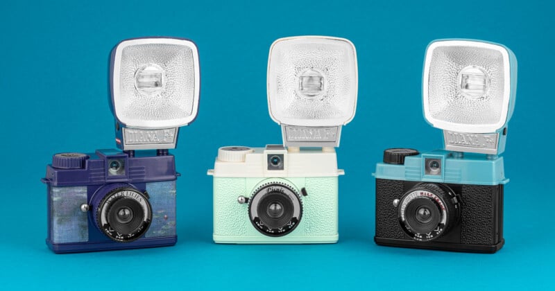 Three vintage-style cameras with flash attachments are displayed against a blue background. The cameras are colored dark blue, light mint, and black, each featuring a retro design with textured exteriors and prominent lenses.