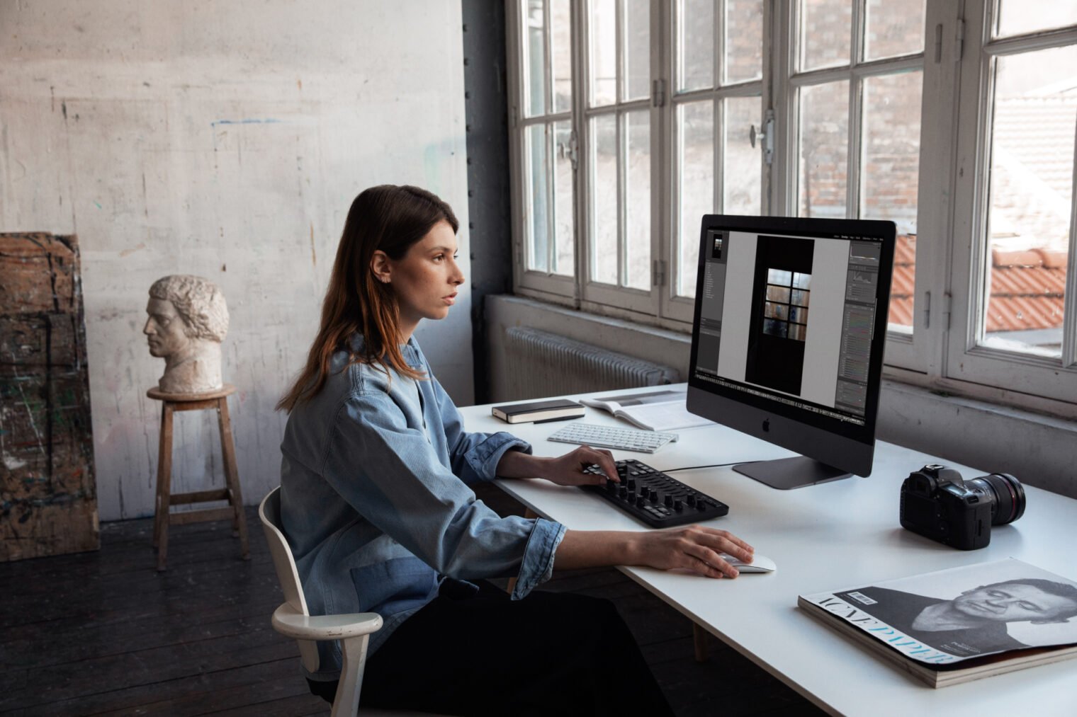 A woman uses the Loupedeck+ photoediting keyboard at a desk.