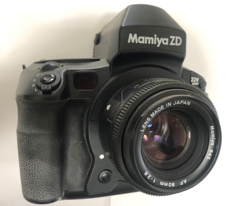 A close-up view of a Mamiya ZD medium format digital camera with an 80mm f/2.8 lens. The lens has "Made in Japan" inscribed on it. The camera is black and features a textured grip on the left side.