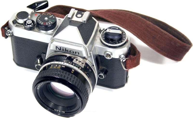 A vintage Nikon film camera with a black and silver body is shown from an angle. The camera is equipped with a lens and has a brown strap attached. The brand name is visible on the front.