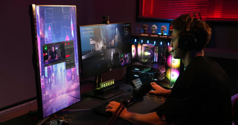 A person is gaming on a computer setup with multiple monitors. The room has dim lighting, neon accents, and gaming equipment. The screens display a game and a video call. The person wears headphones and uses a keyboard and mouse.