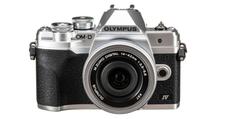 A silver and black Olympus OM-D E-M10 Mark IV camera with a M.Zuiko Digital 14-42mm lens, viewed from the front. The camera features a classic design with various dials and controls on top.