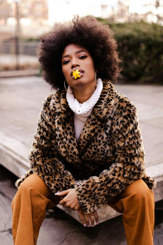 Portrait of young black lady sitting on a sidewalk.