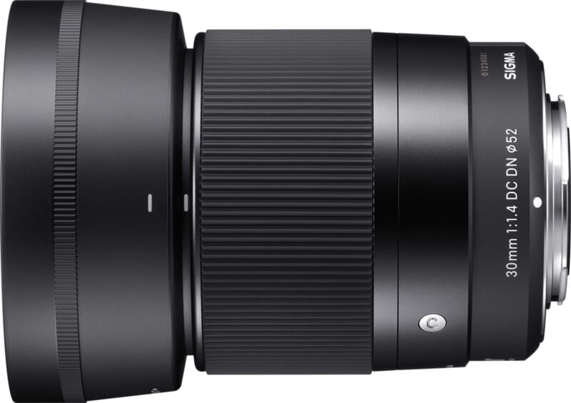 Close-up of a Sigma 30mm f/1.4 DC DN lens in black. The lens is positioned horizontally, showcasing the ribbed focus ring, smooth finish, and lens specifications engraved on the side.