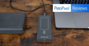 An external storage device connected to a laptop via a USB-C cable is shown on a wooden surface. The image also includes a ProGrade Digital card holder on the left side. The top-right text overlay reads "PetaPixel Reviews.