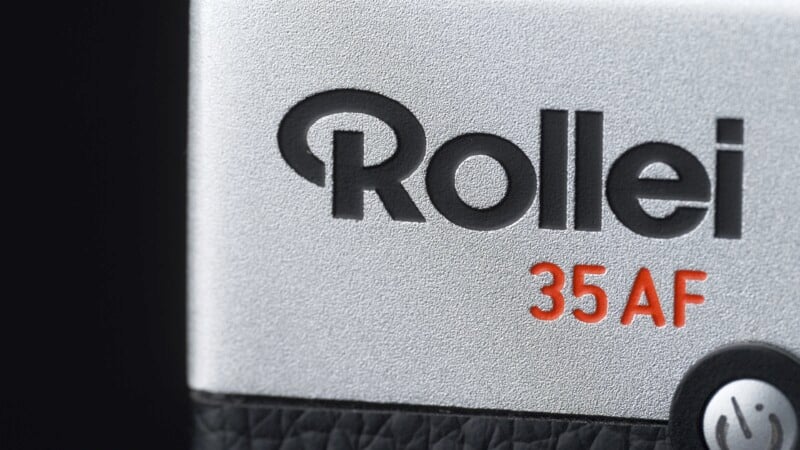 Close-up of a camera with the word "Rollei" in bold black and "35 AF" in red on a silver background. A small part of a button is visible at the bottom right.