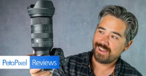 A man with gray-streaked hair and a beard smiles while holding up a DSLR camera with a large lens against a gray background. A banner at the bottom reads "PetaPixel Reviews.