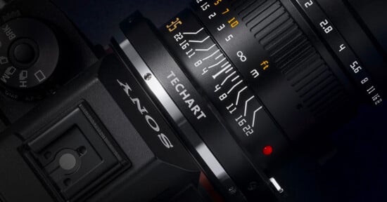 Close-up of a camera with a lens attached, showing detailed focus and aperture markings. The lens displays a brand name "TECHART" and distance indicators. The camera body has part of the "SONY" logo visible. The image emphasizes the technical details of the equipment.