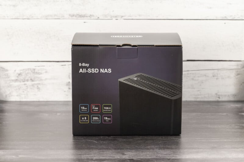 A black box labeled "8-Bay All-SSD NAS" displayed on a dark surface with a light wooden background. The box shows an image of the product and highlights features such as "10 GbE, Tool-Free, 200W, 19 dBA", and "8 x 2.5" bays.