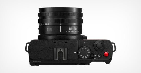 A digital camera viewed from the top, featuring a cylindrical lens with markings "18-40" and "0.5m-0.9ft∞." Controls include a dial, buttons, and a red recording button. The body is black with textured finish, and the Panasonic logo is partially visible.