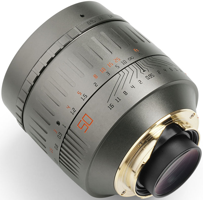 Close-up of a metallic camera lens with a focus ring featuring engraved numbers and distances. The lens has a sleek design with orange markings and a gold-colored mount.