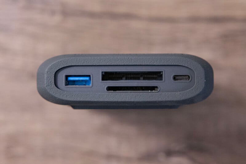 Close-up view of an external hard drive showing various ports on the side. The inputs include a blue USB 3.2 Gen 1 port, two SD card slots, and a USB-C port. The background is a blurred, wooden surface.