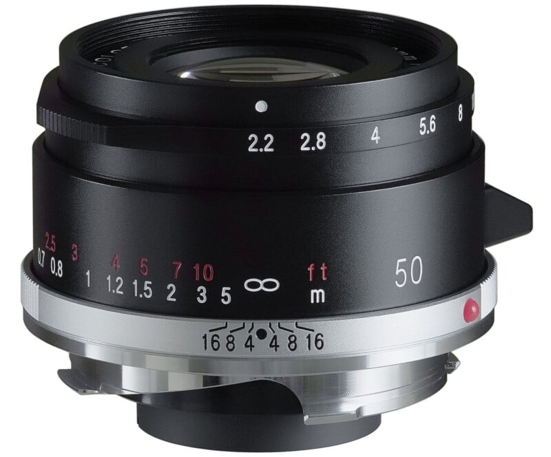 Close-up of a black camera lens with a silver ring. The lens displays various aperture and distance markings, including f-stops from 2 to 16 and a focus range indicator. The lens is marked with the number 50, indicating its focal length.