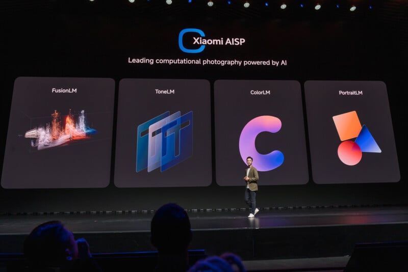 A person stands on a stage presenting at a technology event. Behind them is a large screen displaying the text "Xiaomi AISP - Leading computational photography powered by AI" with four sections labeled FusionLM, ToneLM, ColorLM, and PortraitLM, each with a corresponding graphic.