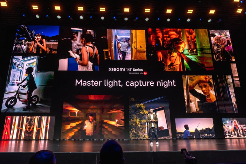 A person stands on a stage presenting the Xiaomi 14T Series. Behind them is a large screen displaying a variety of night-time photographs under the tagline "Master light, capture night." Bright stage lights illuminate the scene.