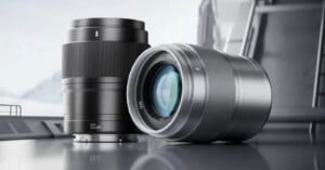 Two camera lenses displayed on a sleek surface. The left lens is marked 35mm and stands upright, while the right lens lies on its side, showcasing its glass element. The background is softly blurred, highlighting the sharpness and design of the lenses.