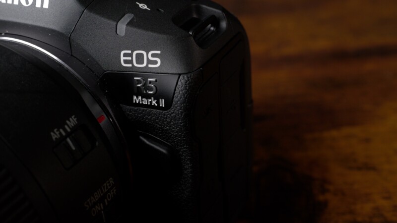 Close-up of a black Canon EOS R5 Mark II camera body, showcasing its branding and textured grip on a wooden surface.